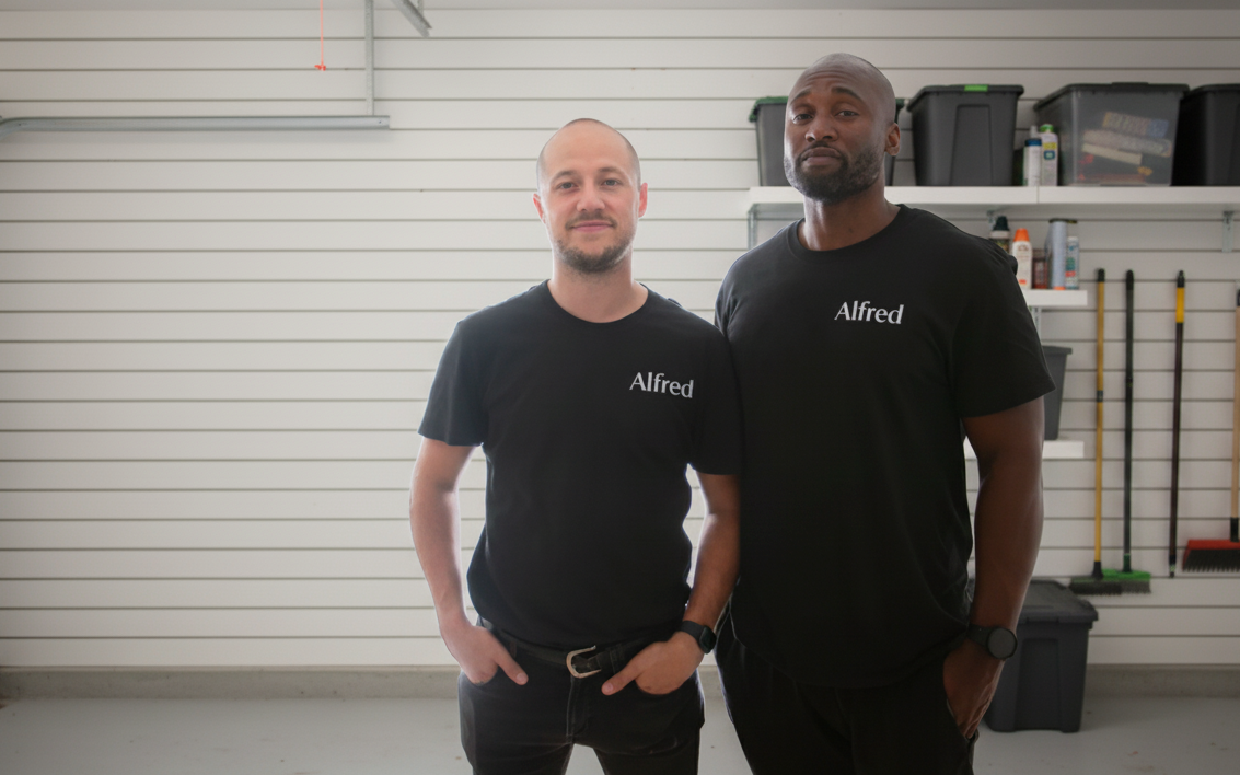 Two men wearing black t-shirts with 'Alfred' logo in a garage setting.